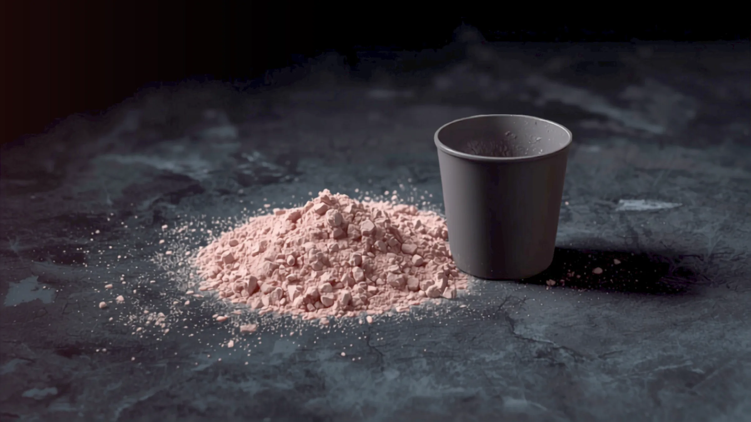 Kasa vaaleanpunaista pre workout -jauhetta ja tumma mittalusikka tummalla pinnalla.